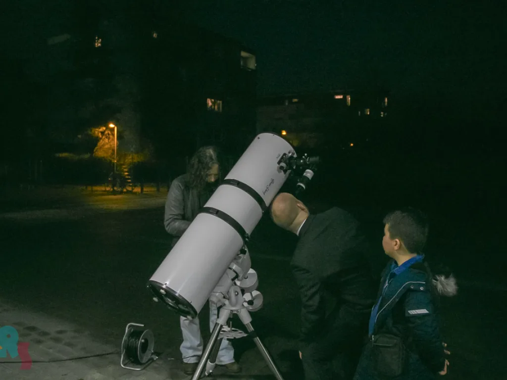 Besucher schauen abends durch ein Teleskop.